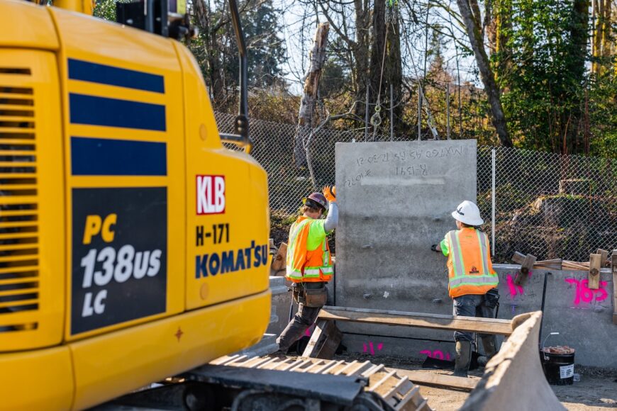 F200 wall crew installing MSE panel that an excavator is placing