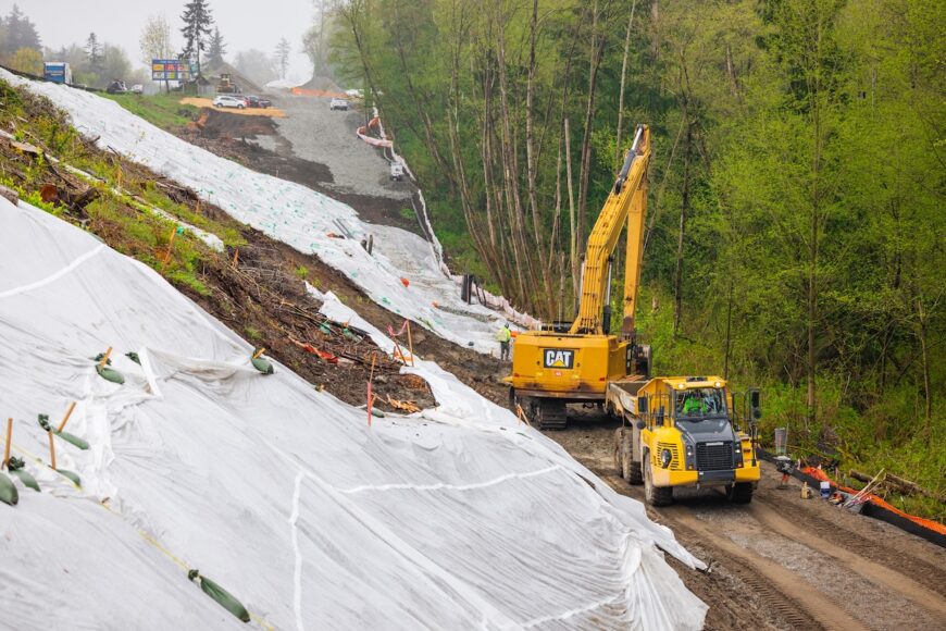 F200 excavator and haul truck working at base of hillside that is covered in plastic