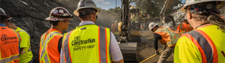 Crews grading and working while excavators excavating trench where culvert will be installed